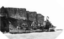 Image : L'HMS Fury, échoué et ayant heurté une mine, attend d'être remorqué devant les falaises d'Arromanches