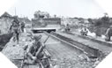 Image : Un Sherman Bulldozer traverse le pont d'Airel le 8 juillet avec des soldats du 105e Engineer Combat Batalion Américain