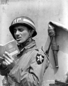 June 15, 1944: First class Rocco Festa of the Military Police of the 2nd Infantry Division consults the guide on France and the French aboard SS John Hay. Photo: US National Archives