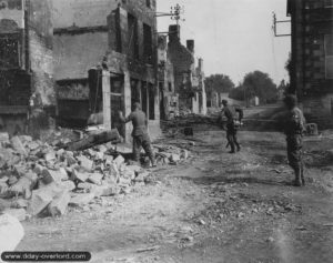 Le 8 août 1944, des prisonniers allemands déblaient les ruines, surveillés par la police militaire de la 2nd Armored Division à Barenton. Photo : US National Archives