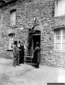 19 juin 1944 : des habitants de Cerisy-la-Forêt plantent un drapeau français devant la porte d’entrée de leur maison. Photo : US National Archives