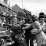 8 août 1944 : des soldats américains à côté d’une Jeep savourent un repas offert par la population de Champigné en liesse après sa libération. Il s’agirait du Captain Phillip C. Staples de la compagnie G, 2nd Infantry Regiment, 5th Infantry Division. Photo : US National Archives