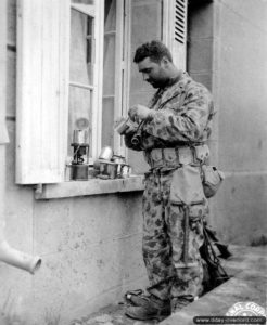 Juillet 1944 à Dangy : le soldat américain Joseph De Freitos appartenant au 41st Armored Infantry Regiment de la 2nd Armored Division fait chauffer sa ration sur un réchaud individuel. Noter sa tenue bariolée, peu utilisée pendant la bataille de Normandie. Photo : US National Archives