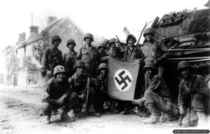 20 août 1944 : des soldats américains appartenant au 359ème régiment de la 90ème division d’infanterie posent fièrement devant l’épave d’un char allemand abandonné et avec un drapeau pris à l’ennemi à Fel. Photo : US National Archives