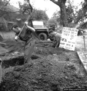 Le transmetteur canadien Rusty Forsythe et son capitaine R. W. Armstrong devant un écriteau en anglais indiquant : "Les Anciens ne meurent pas, ils creusent ! Et disparaissent dans une tranchée de tir". Photo : US National Archives