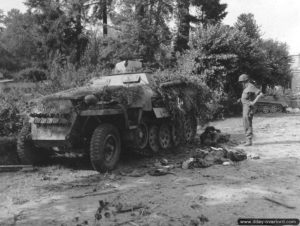 Un soldat américain, armé d’un M3 Grease Gun, observe le cadavre d’un soldat allemand tombé à proximité d’un SdKfz 251 Ausf. D. appartenant à la 1.SS-Panzer-Division à Le Neufbourg. Photo : US National Archives