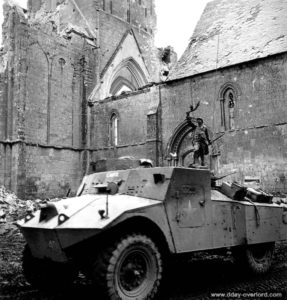 4 juillet 1944 : une auto-mitrailleuse Morris Light Reconnaissance Car MK II « Carol » devant l’église en ruine de Norrey-en-Bessin et son monument aux Morts de la Première Guerre mondiale. Photo : US National Archives