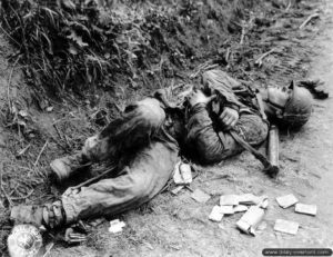 Le corps d’un soldat allemand de la Waffen S.S. en tenue de camouflage M43 dans le bas côté d’un chemin du secteur de Quibou. Il porte un canon de rechange dans sa housse de transport pour mitrailleuse MG 42. Photo : US National Archives