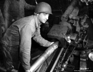 11 juillet 1944 : dans le secteur de Saint-Georges-d’Elle, le soldat de première classe Anthony Tony Andenucio pose à l’occasion du tir par son régiment du 50 000ème obus de 105 mm HM2. Photo : US National Archives