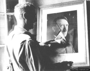 17 juin 1944 : le soldat Laurence devant le portrait d’Adolf Hitler dans un bâtiment occupé par les Allemands à Sainte-Mère-Eglise. Photo : US National Archives