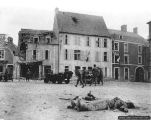 15 juin 1944 : des soldats accompagnés de Jeep de la police militaire sur la place du marché de Trévières où un soldat allemand du 916. Infanterie-Regiment de la 352. Infanterie-Division a été tué. Photo : US National Archives