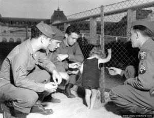 Sur la plage de Trouville-sur-Mer, devant le Casino, des soldats partagent des friandises avec un jeune enfant très intimidé. Photo : US National Archives