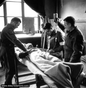 27 juin 1944 : le capitaine Earl Bourbonnais, le sergent T. F. McFeat et le soldat J. Viner soignent un blessé à Basly. Photo : US National Archives