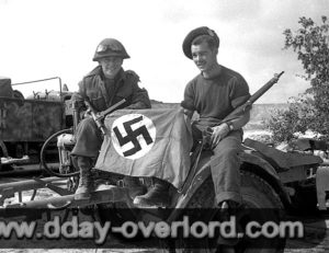 10 août 1944 : les soldats L. B. Roy et R. L. Parker du Queen’s Own Cameron Highlanders of Canada, 6th Infantry Brigade, 2nd Canadian Infantry Division, posent avec un drapeau nazi pris à l’ennemi. Photo : US National Archives
