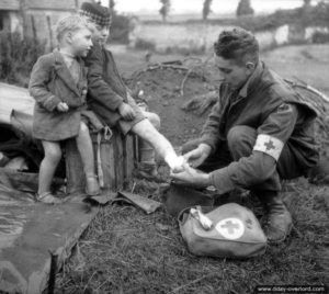 19 juin 1944 : le première classe J. W. Curtis du service de santé canadien soigne la jambe brûlée de Marcel à côté de son frère Daniel à 19 juin 1944 : les deux frères Frémont : Marcel, 10 ans (qui porte le calot canadien) et son frère Daniel, 4 ans à Colomby-sur-Thaon. Photo : Library and Archives Canada