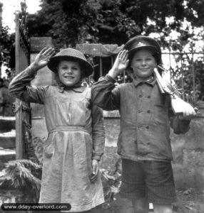 27 juin 1944 : les frères Guy (10 ans) et Michel (13 ans) Pierre saluent fièrement avec des attributs canadiens. Photo : US National Archives