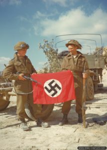 10 août 1944 : les soldats L. B. Roy et R. L. Parker du Queen’s Own Cameron Highlanders of Canada, 6th Infantry Brigade, 2nd Canadian Infantry Division, posent avec un drapeau nazi pris à l’ennemi. Photo : US National Archives
