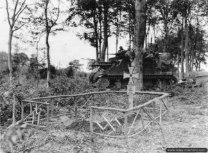 Un canon automoteur M7 Priest américain longe la tombe du S.S. Unterscharführer Josef Richtsfeld tué le 17 juin 1944 dans le secteur de Saint-Gilles. Photo : US National Archives