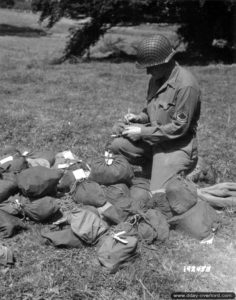 9 août 1944 : à Saint-Manvieu-Bocage, un sous-officier appartenant à une unité de suivi des pertes (Grave Registration Service) renseigne les étiquettes des effets personnels à renvoyer. Photo : US National Archives