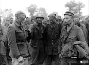 22 août 1944 : des prisonniers allemands de différentes origines aux côtés d’un policier militaire américain dans le camp de Nonant-le-Pin. Photo : US National Archives