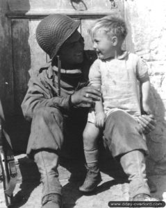 23 juin 1944 : le soldat Fred Linden amuse un jeune garçon de Trévières. L'identité du garçon a fait l'objet d'importants débats en 2017, deux personnes s'étant reconnues simultanément : Gérard Poincheval et Marcel Castel. Le mystère quant à sa véritable identitée demeure. Photo : US National Archives