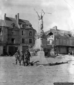 15 juin 1944 : les parachutistes Charles E. Rinehart et Charles A. West du 506th Parachute Infantry Regiment, le sergent James V. Longane du 327th Glider Infantry Regiment devant le monument aux Morts de Carentan. Photo : US National Archives