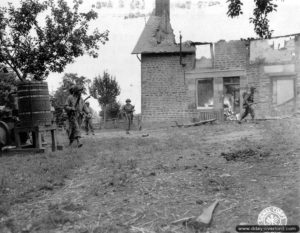 Des soldats américains progressent devant une maison qui termine de se consumer à Juvigny-le-Tertre. Photo : US National Archives