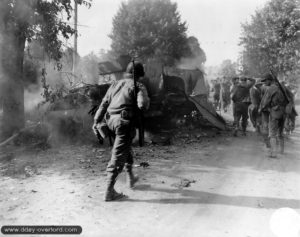 Un soldat américain escorte des prisonniers allemands dans le secteur d'Avranches. Ils passent à côté de l’épave d’un Half-Track M3A1. Photo : US National Archives