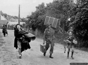 8 juin 1944 : à l'entrée de Sainte-Mère-Eglise, le parachutiste C. C. Hayes de la Fox Company du 505th PIR, 82nd Airborne, apporte son aide à Madame Digeon et Jacques Birette qui fuient les combats. Hayes est tué en Hollande le 20 septembre 1944. Photo : US National Archives