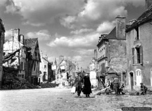 Place Saint-Gervais, le soldat canadien A. Mallais aide une dame âgée de Falaise à porter des affaires. Photo : US National Archives