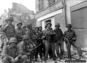 Des soldats du 317ème régiment de la 80ème division d’infanterie américaine dans la rue Saint-Germain à Argentan, écoutent le soldat H. C. Medley jouer à l’accordéon. Photo : US National Archives