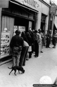 8 juillet 1944 : des civils observent les actualités militaires en photos dans une vitrine à Cherbourg. Photo : US National Archives