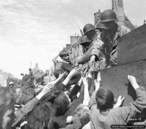 28 juin 1944 : la population reçoit des friandises de la part des soldats américains à bord d’un Half-Track M3A1 à Isigny-sur-Mer. Photo : US National Archives