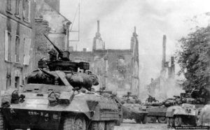 19 juillet 1944 : une auto-mitrailleuse M8 du 29th Reconnaissance Squadron Mechanized de la 29ème division d’infanterie sur la Place Sainte-Croix à Saint-Lô. Photo : US National Archives