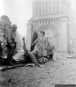 Une habitante de Trévières et un soldat de la police militaire devant le monument aux Morts de la Première Guerre mondiale, tombé suite aux bombardements. Photo : US National Archives