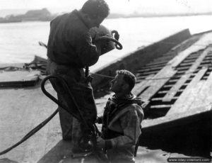 9 mars 1945 : à Cherbourg, le sergent américain Joseph B. Piccardella s’apprête à aider le scaphandrier anglais Edgar B. Moore à mettre son casque. Photo : US National Archives