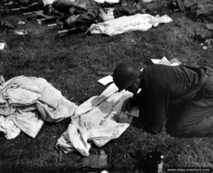 Sur l'un des cimetières provisoires de Sainte-Mère-Eglise, un membre de la compagnie de suivi des pertes (Graves Registration Company) rédige le nom d’un soldat tué au combat sur un linceul : PFC Frederick R Smith. Photo : US National Archives