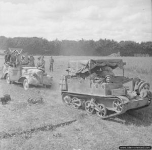 21 août 1944 : un Universal Carrier du Royal Horse Artillery tracte un véhicule allemand dans le secteur d’Argentan et l’équipage anglais exhibe les drapeaux à croix gammée de prise. Photo : IWM