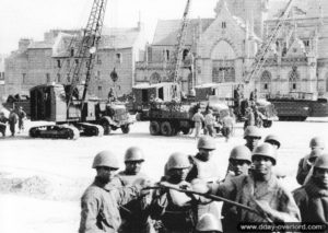 Place Napoléon à Cherbourg, des grues sur chenilles sont alignées pour effectuer des déchargements. Au premier plan, des soldats américains noirs chargés du suivi et des opérations logistiques. Photo : US National Archives