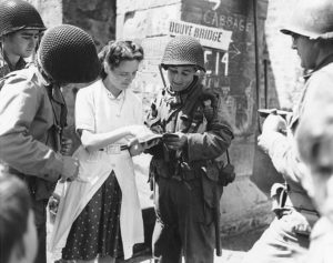 12 juin 1944 : Marie-Esther Duchenes, volontaire de la Croix Rouge avec des personnels d’une Engineer Special Brigade devant la fontaine de Sainte-Marie-du-Mont. Photo : US National Archives
