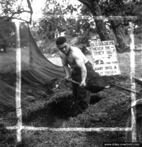 Le sergent Reg Hannigan Forsythe creuse un trou de combat devant un écriteau en anglais indiquant : "Les Anciens ne meurent pas, ils creusent ! Et disparaissent dans une tranchée de tir". Photo : US National Archives
