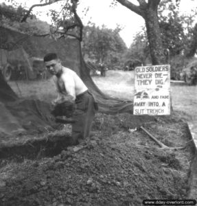 Le sergent Reg Hannigan Forsythe creuse un trou de combat devant un écriteau en anglais indiquant : "Les Anciens ne meurent pas, ils creusent ! Et disparaissent dans une tranchée de tir". Photo : US National Archives