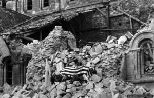 20 juillet 1944 : le corps du Major Thomas D. Howie, commandant le 3ème bataillon du 116ème régiment de la 29ème division d’infanterie a été déposé sur les ruines de l’église Sainte-Croix et recouvert de la bannière étoilée. Photo : US National Archives