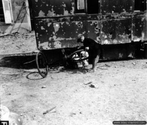 Place Jeanne d’Arc, un enfant tente de réparer une bicyclette à Montebourg. Photo : US National Archives