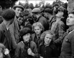 Des civils se pressent au contact des parachutistes américains dans le secteur de Carentan alors que des avions patrouillent dans le ciel. Photo : US National Archives