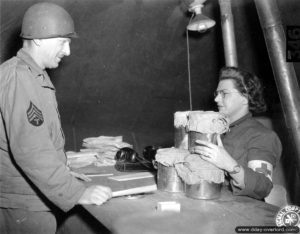 Une infirmière remet des récipients à un Technical Sergeant américain dans une tente médicale du secteur de Carentan. Photo : US National Archives