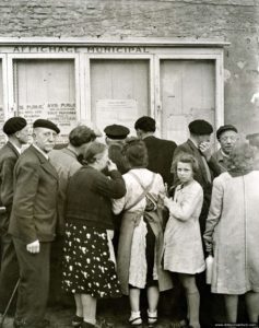Des habitants de Courseulles consultent les messages des Alliés mis à l'affichage. Photo : Archives Canada