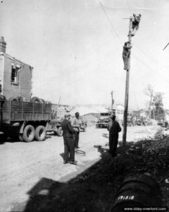 Des civils français sont réquisitionnés pour réparer les lignes électriques dans Carentan. Photo : US National Archives