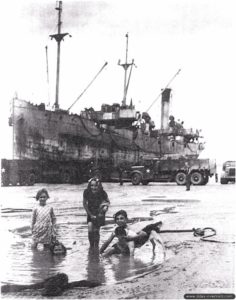 De jeunes normands jouent à marée basse devant un caboteur en cours de déchargement à Port-en-Bessin. Photo : IWM