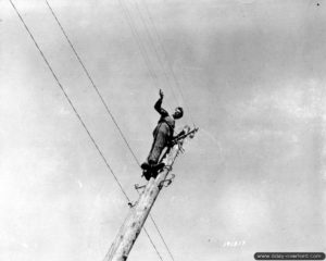 Des civils français sont réquisitionnés pour réparer les lignes électriques dans Carentan. Photo : US National Archives